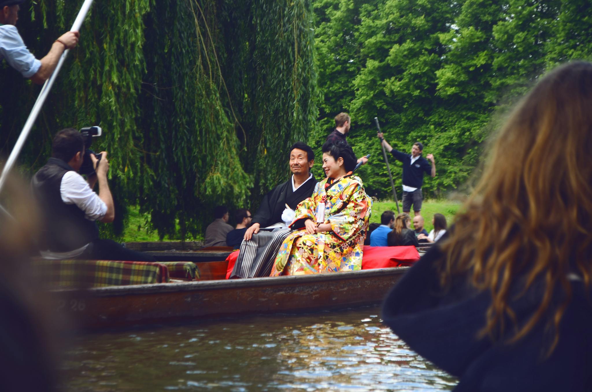 A couple in traditional kimono enjoys a scenic outdoor boat ride while being photographed.
