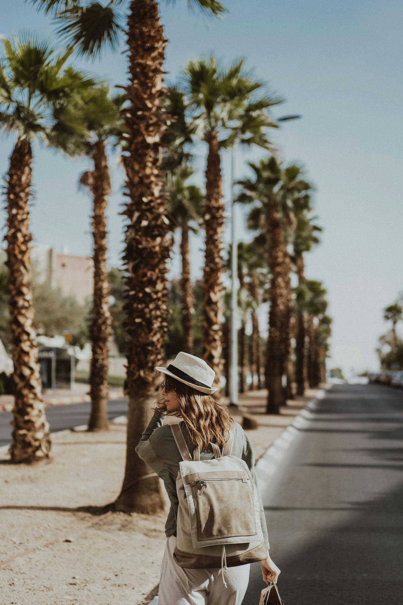 A woman walks down a palm tree lined street in Eilat, Israel during summer, evoking a tropical vacation feel.