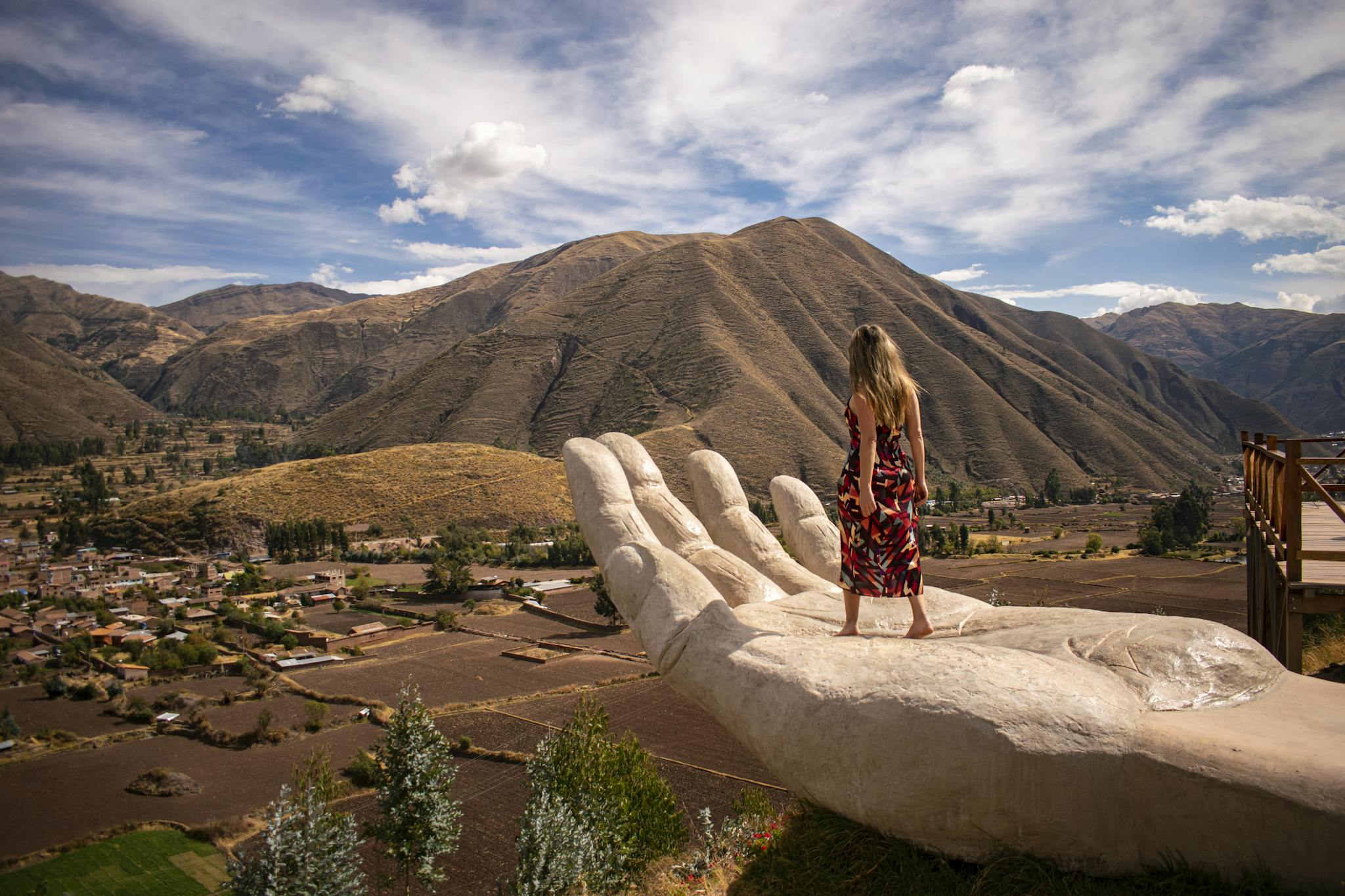 Woman stands on giant hand sculpture in Huaro, overlooking Peruvian landscape.